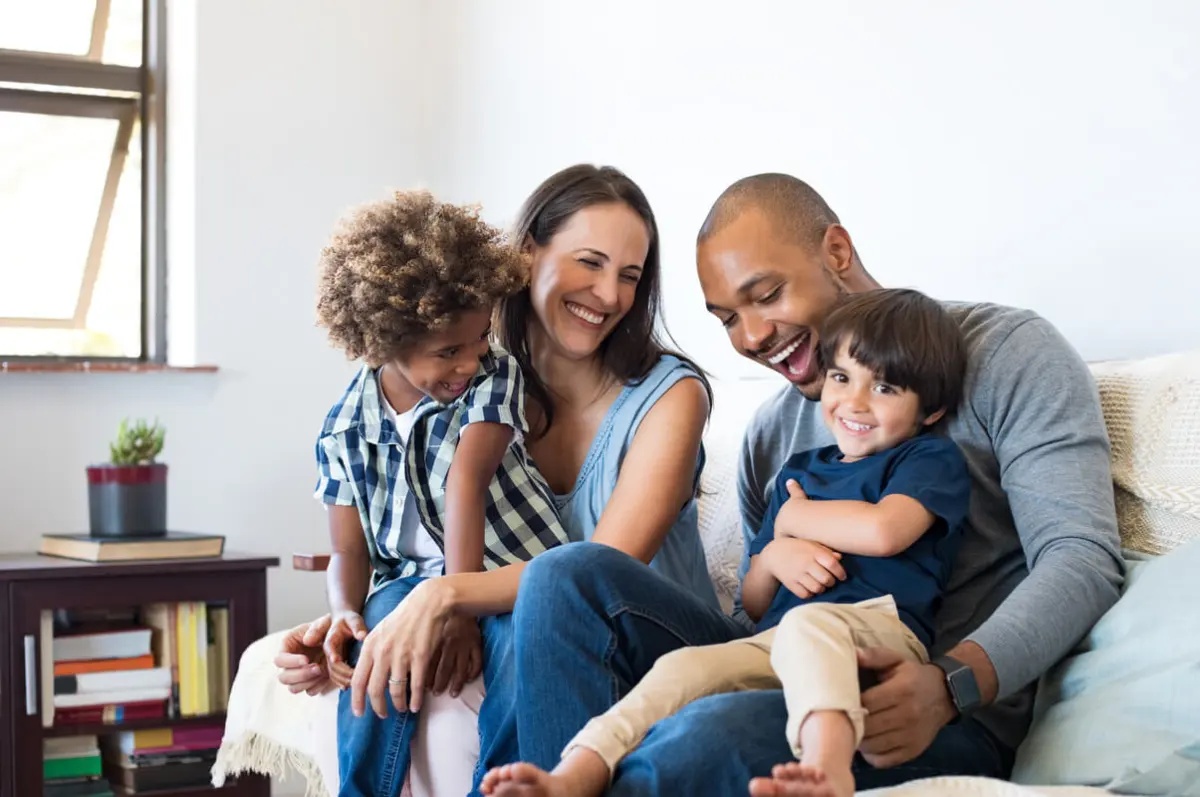 A smiling family of four sitting together on a couch at home